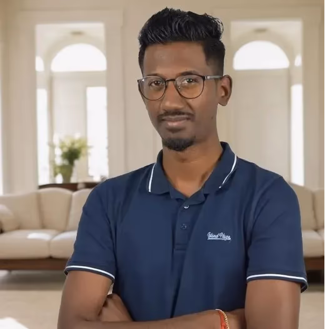 Man with glasses and short hair wearing a navy blue polo shirt standing with arms crossed in a bright living room.